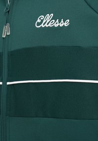 Zöld zipzáras dzseki fehér részletezéssel és az "Ellesse" emblémával hímzéssel a bal felső részen, texturált anyagból készült.