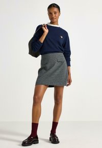 Marineblå sweatshirt med ribbet krave og lille hjerte-logo. Gråternet nederdel med to frontlommer. Bourgogne sokker og sorte loafers afslutter outfittet.