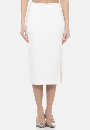 Donna che indossa una gonna midi a matita bianca con spacco laterale e dettaglio di cintura metallica, abbinata a scarpe con il tacco taupe.