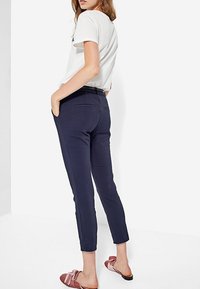 Granatowe, zwężane spodnie wykonane z gładkiej tkaniny, z bocznymi kieszeniami i eleganckim krojem. Połączone z różowymi wsuwanymi butami z kokardką.