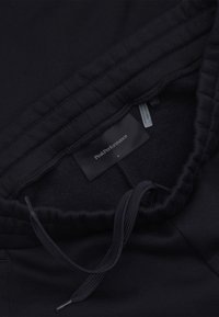 Zwarte tunnelkoord tailleband van een kledingstuk met het Peak Performance merklabel en een klein maatlabel binnenin de tailleband.