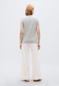 Γκρι μπλουζάκι με κοντά μανίκια και ελαφρώς κυρτή ραφή, συνδυασμένο με εκρού παντελόνι φαρδιάς γραμμής, με ομαλή υφή και διακριτικό σχέδιο τσιπουριάς.