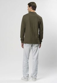 Långärmad olivgrön skjorta i mjukt tyg, med avslappnad passform och enkel halsringning, kombinerad med ljusblå jeans.