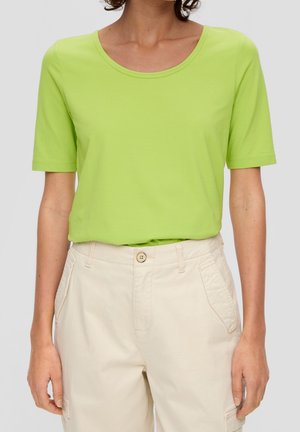 Person iført en kortærmet limegrøn skjorte, der er stukket i højhøjede beige bukser med knap og frontlommer.