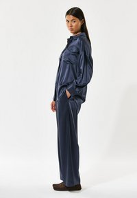 Marineblå satin oversized skjorte med to brystlommer, parret med matchende viddebukser og brune mokkasiner.