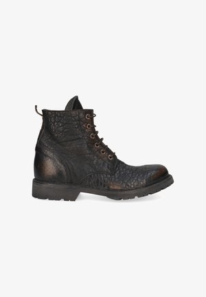 Bottine en cuir noir avec surface texturée, bout rond, semelle en caoutchouc et sept œillets. Elle est équipée d'une languette à l'arrière.