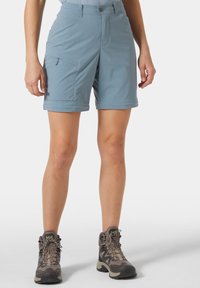 Vaaleansiniset ulkohousut, joissa on vetoketjullinen tasku ja istuva malli. Yhdistetty ruskeisiin vaelluskenkiin, joissa on teksturoitu pinta.