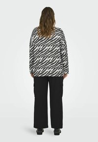 Maglia a maniche lunghe grigia chiara con strisce zebrate nere, abbinata a pantaloni cargo neri a gamba larga con tasche laterali.