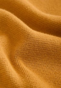 Tessuto lavorato a maglia di colore giallo senape, con una trama fine e un sottile motivo a coste, con una sensazione morbida e leggermente elasticizzata.