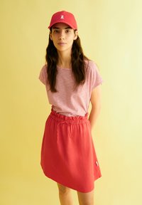 Gorro rojo y camiseta a rayas combinados con una falda roja de cordón. Textura suave, ajuste casual. El fondo es de un color amarillo claro sólido.