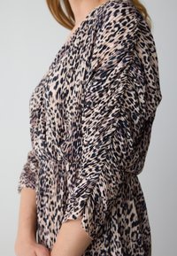 Leopardenmuster-Kleid aus leichtem, plissiertem Stoff; mit langen Ärmeln, tiefem V-Ausschnitt und gerafftem Taillenbereich für eine fließende Silhouette.