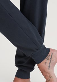Marine joggerpants gemaakt van zachte stof, met een taps toelopend ontwerp en elastische boorden bij de enkels. Zichtbare huid en tatoeages op de voeten.