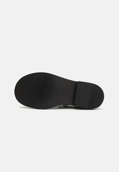Suela de zapato negra con un acabado suave, que presenta un tacón elevado y un patrón de agarre texturizado. Las marcas incluyen el nombre de la marca y la talla.