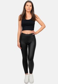 Outfit composto da un crop top nero e leggings neri a vita alta, realizzati in materiale liscio e lucido. Abbinato a sneakers bianche, in piedi contro uno sfondo neutro.