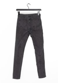 Jeans ajustados de mezclilla negra, con un diseño clásico de cinco bolsillos, una textura sutil y una cinturilla de altura media, colgados de una percha negra.