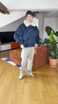 Marineblauwe bomberjack met een crèmekleurige nepbont kraag, elastische mouwen en zoom. Lichtgrijze broek en zilveren sneakers maken de look compleet.