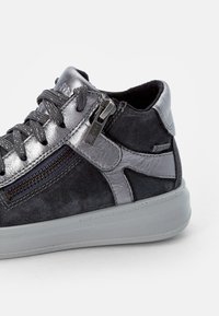 Graue Wildleder-Sneaker mit einem metallischen Reißverschlussakzent, strukturierten Schnürsenkeln und einer glatten Gummisohle. Auffälliges wasserdichtes Etikett an der Seite.