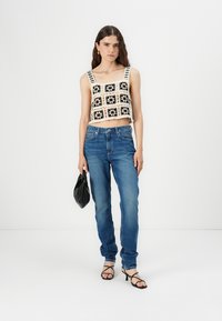 Top corto de ganchillo con un patrón floral en blanco y negro, combinado con jeans rectos azules y tacones negros atados. Accesorio: bolso pequeño negro.