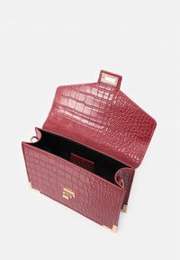 Torebka skórzana w kolorze czerwonym z wytłoczonym wzorem krokodyla, z zapięciem w kolorze złotym; otwiera się na przestronną czarną wnętrze; posiada kanciastą formę oraz złote akcenty metalowe.