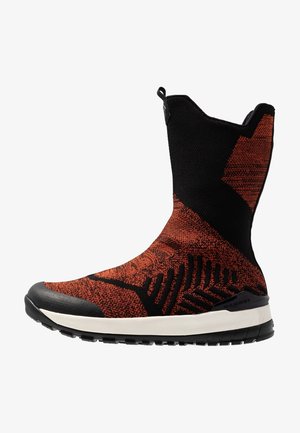 Bota de punto hasta el tobillo con diseño en naranja y negro, puntera reforzada y suela texturizada para mayor agarre. Diseño flexible y ligero.