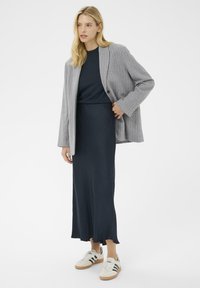 Pelēka pinstripe žakete virs tumši zila augšdaļa un gara tumši zila svārku, apvienota ar baltām sneakers ar melnām svītrām un koka zole.