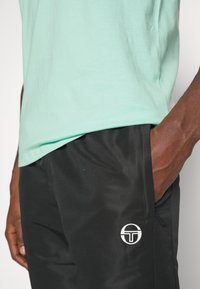 Mintgroene T-shirt met korte mouwen, gecombineerd met zwarte mesh shorts met een wit logo aan de onderlinkerkant.