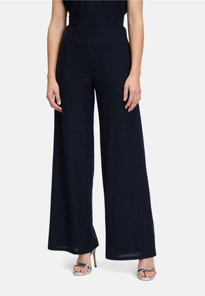 Pantaloni a gamba larga in tessuto blu navy, con una texture liscia e vita alta. Indossati con sandali con tacco metallici.