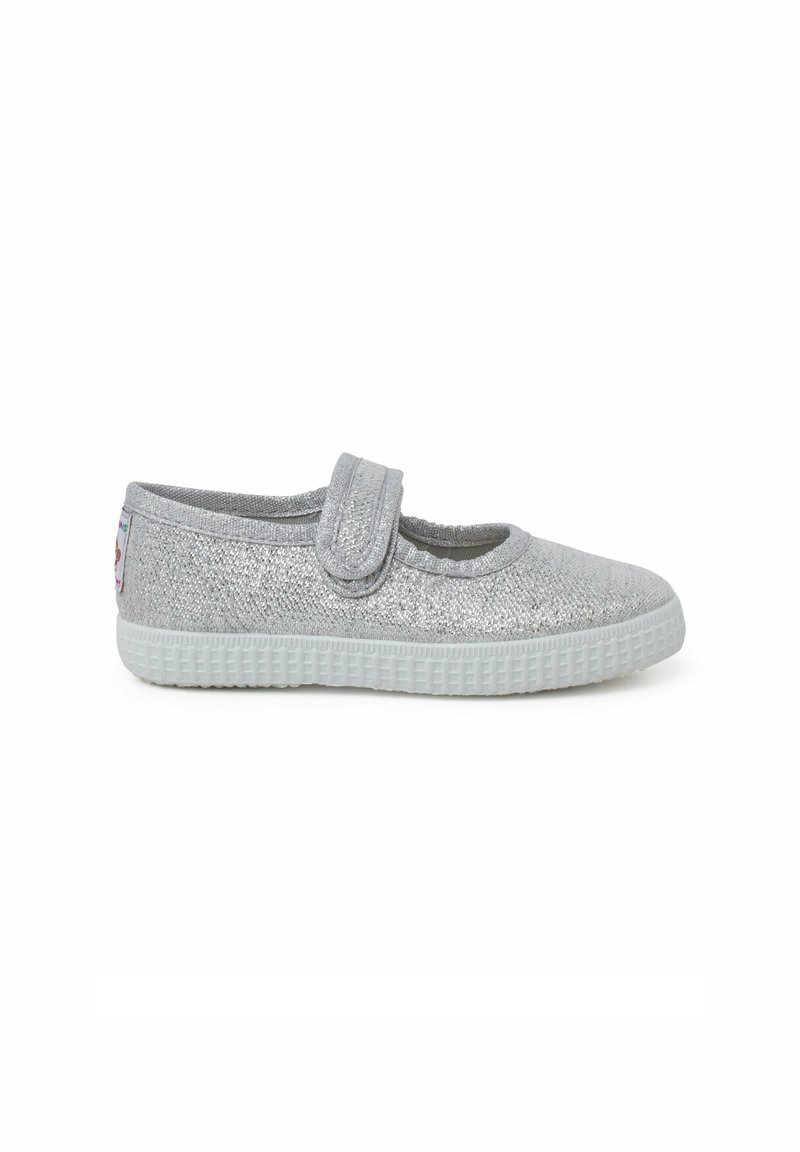 Chaussure Mary Jane argentée pailletée avec une bride velcro, bout arrondi et semelle en caoutchouc texturée. Accents décoratifs sur le talon.