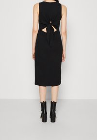 Robe midi noire sans manches avec un détail à nouer dans le dos, découpes au niveau de la taille, faite d'un tissu doux ; associée à des bottes noires à talons épais.
