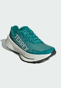 Turkusowy but sportowy z siateczkowym wierzchem, białym logo "TERREX", teksturowanym wzorem, amortyzowaną podeszwą środkową i czarną gumową podeszwą.