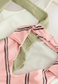 Gros plan superposé de deux sacs en tissu, l’un vert clair et l’autre rose avec des rayures marron et blanches, sur une surface blanche.