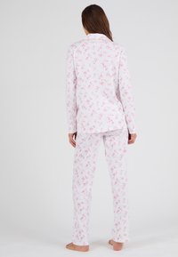 Ensemble de pyjama blanc avec un motif floral rose, comprenant un haut à manches longues et boutons ainsi qu'un pantalon assorti. En tissu en coton, coupe décontractée.