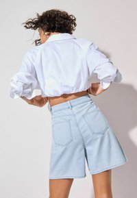 Cropped white shirt with puffed sleeves paired with light blue denim shorts featuring two back pockets and a relaxed fit.