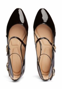 Zapatos Mary Jane de charol negro con punteras puntiagudas, correas cruzadas y herrajes en tono dorado. Interior suave con un mínimo logo en relieve.