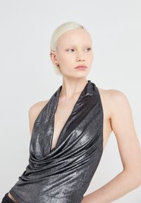 Metallic sølv halterneck-top med draperet udskæring og glat tekstur, der har en dyb V-formet front og ærmeløs design.