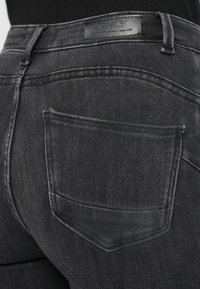 Μαύρο τζιν παντελόνι με ξεθωριασμένο φινίρισμα, με πίσω τσέπη και ετικέτα με το λογότυπο στη μέση. Η υφή φαίνεται λεία και ανθεκτική.