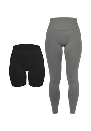 Frau trägt graue Leggings mit hoher Taille und passendes cropped Top, steht aufrecht mit locker hängenden Armen, trägt weiße Sneakers.