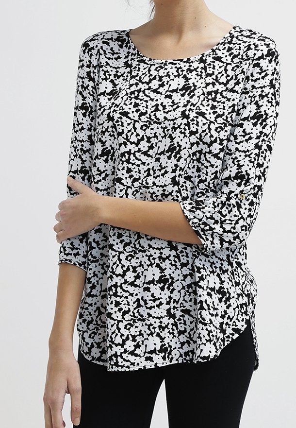 Blusa bianca e nera con una vestibilità morbida, caratterizzata da un collo rotondo e maniche a tre quarti. Il tessuto presenta un motivo maculato.
