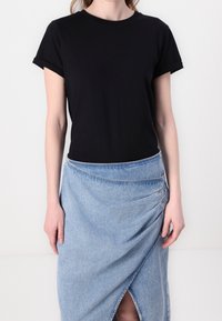 Svart t-shirt med kort ärm i kombination med en ljusblå denimomslagskjol med en gather-design och slitsdetalj. Mjukt tyg med behaglig textur.