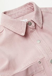Col de chemise en denim rose clair avec boutons-pression argentés et coutures visibles sur la patte de boutonnage avant et le bord de la poche.