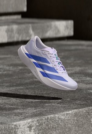 Weißer Laufschuh mit blauen Streifen schwebt über Betontreppen mit Schatten darunter.