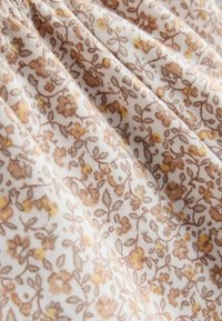 Floraler Stoff mit cremefarbenem Hintergrund, der kleine braune und gelbe Blumen zeigt. Weiche Textur, gerafftes Design und zarte Blättermuster.