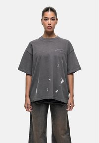 Przesadzona szara koszulka z miękkiej bawełny, z okrągłym dekoltem, z białymi przetarciami i nadrukowanym logo na klatce piersiowej.