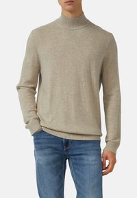 Beiger Rollkragenpullover aus weichem Strickmaterial, mit gerippten Bündchen und Saum, über blauen Jeans getragen.