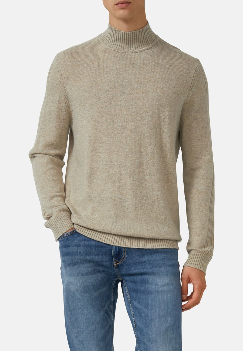 Beiger Rollkragenpullover aus weichem Strickmaterial, mit gerippten Bündchen und Saum, über blauen Jeans getragen.