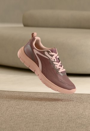 Lichtroze en mauve lichtgewicht sportschoen met een bovenwerk van mesh en een rubberen zool, zwevend in de lucht boven een beige tapijt in een binnenruimte.