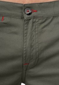 Olijfgroene katoen broek met rode stiksels, een metalen knoop met branding en een rechte snit met platte voorzakken.