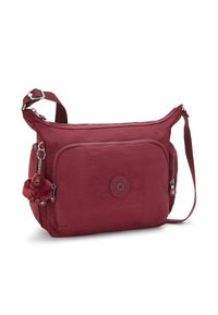 Röd crossbody-väska med justerbar rem, framfick med dragkedja, sidofickor och en liten plyschapa som nyckelring fäst.