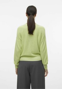 Suéter de punto verde claro con hombros caídos, textura acanalada y mangas largas, combinado con pantalones de pierna ancha grises.