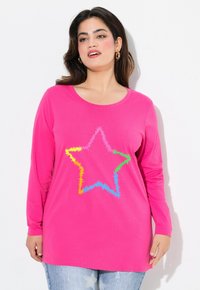 Camiseta de manga larga rosa con un diseño de estrellas multicolores en un patrón texturizado de zigzag, combinada con unos vaqueros de mezclilla de color azul claro con estampado de estrellas.